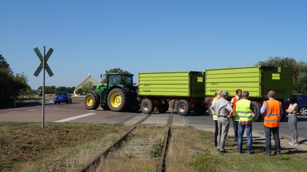 Traktor fährt über Bahnübergang, Menschengruppe schaut zu